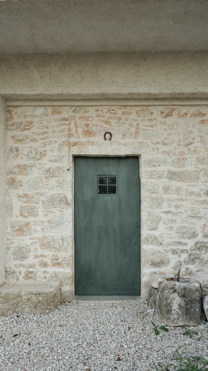 The green cellar door set into the stone wall, a horseshoe fixed above the lintel