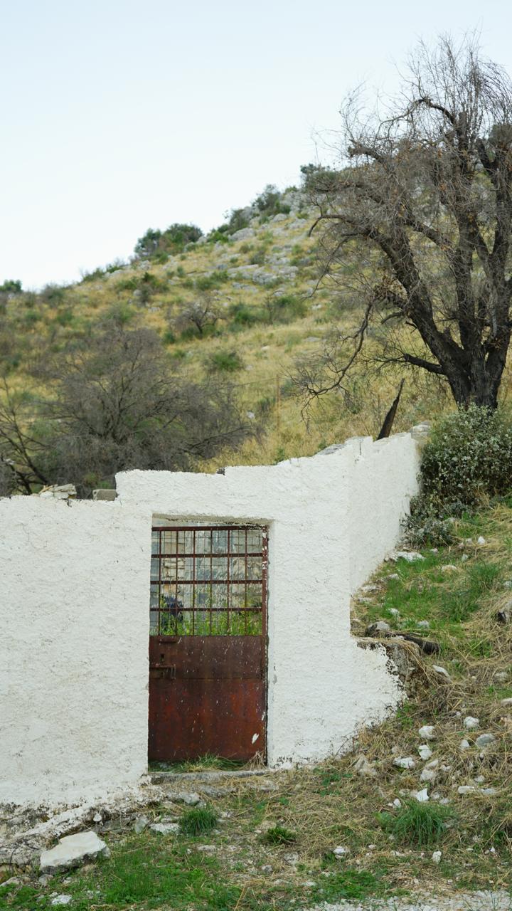 An old rusted iron gate in the whitewashed boundary wall, scrubland hills rising beyond